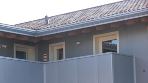 A building with a grey facade, a balcony, and a tiled roof. - Affittacamere Dormire Caldi (Borgo Valbelluna)