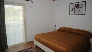 A bedroom with a bed, a window with curtains, a framed picture on the wall, and a wooden ceiling. - Affittacamere Dormire Caldi (Borgo Valbelluna)