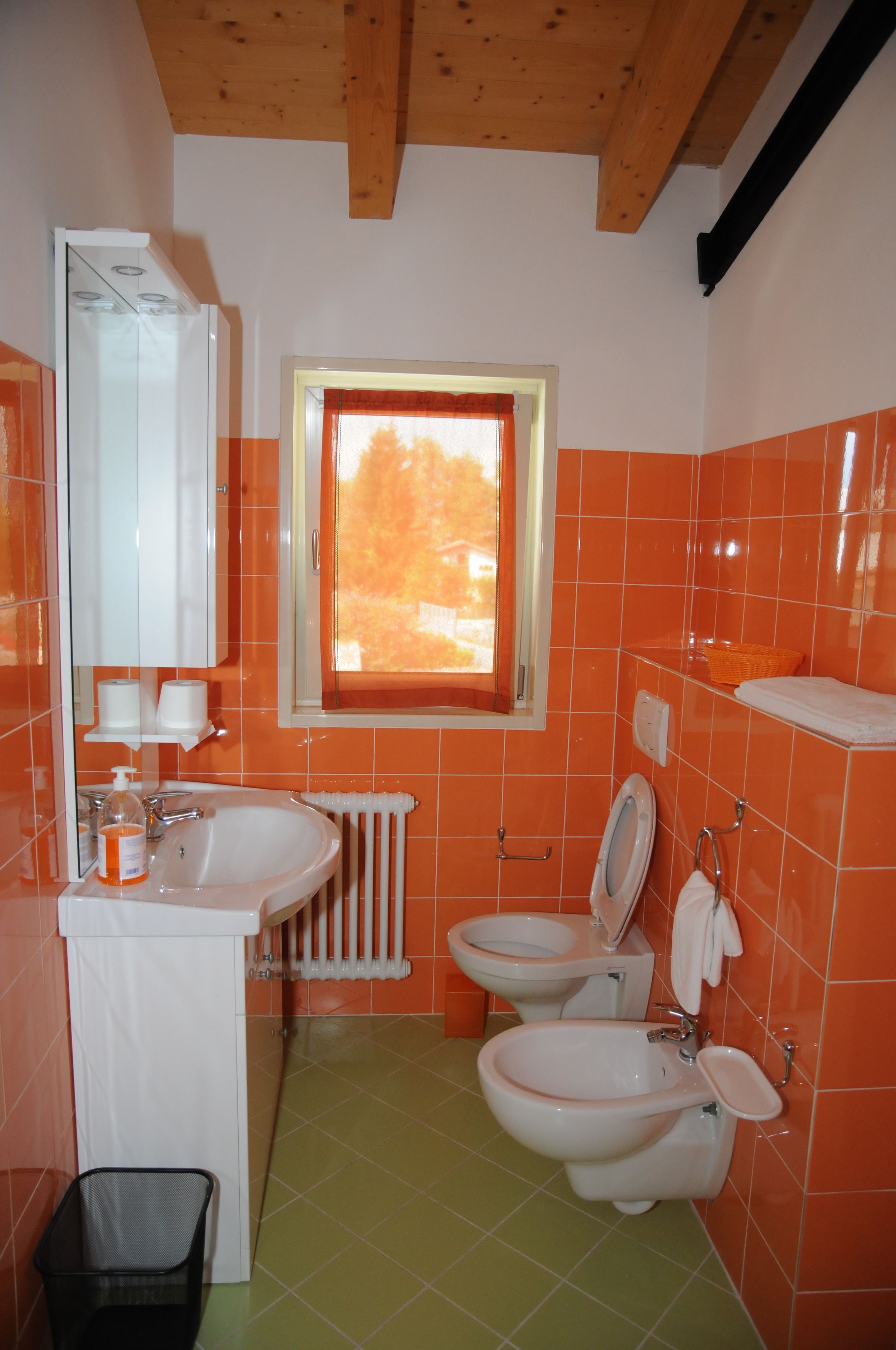 A bathroom with orange tiles, a white sink, two bidets, a window, and a radiator.