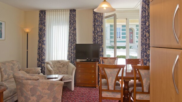 Una sala de estar amoblada con sofá, televisión, mesa de comedor con sillas y refrigerador.