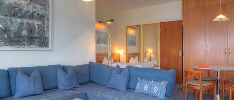 A modern living room with a blue sofa, a glass coffee table, and a dining area with a wooden table and chairs.