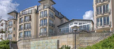 A multi-story hotel with balconies, a stone facade, and a sign indicating the name and location.