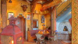 A cozy interior with a checkered bench, wicker chairs, a stone oven, and a staircase with a wooden railing.