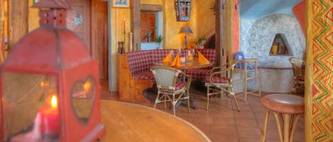 A cozy interior with a checkered bench, wicker chairs, a stone oven, and a staircase with a wooden railing.