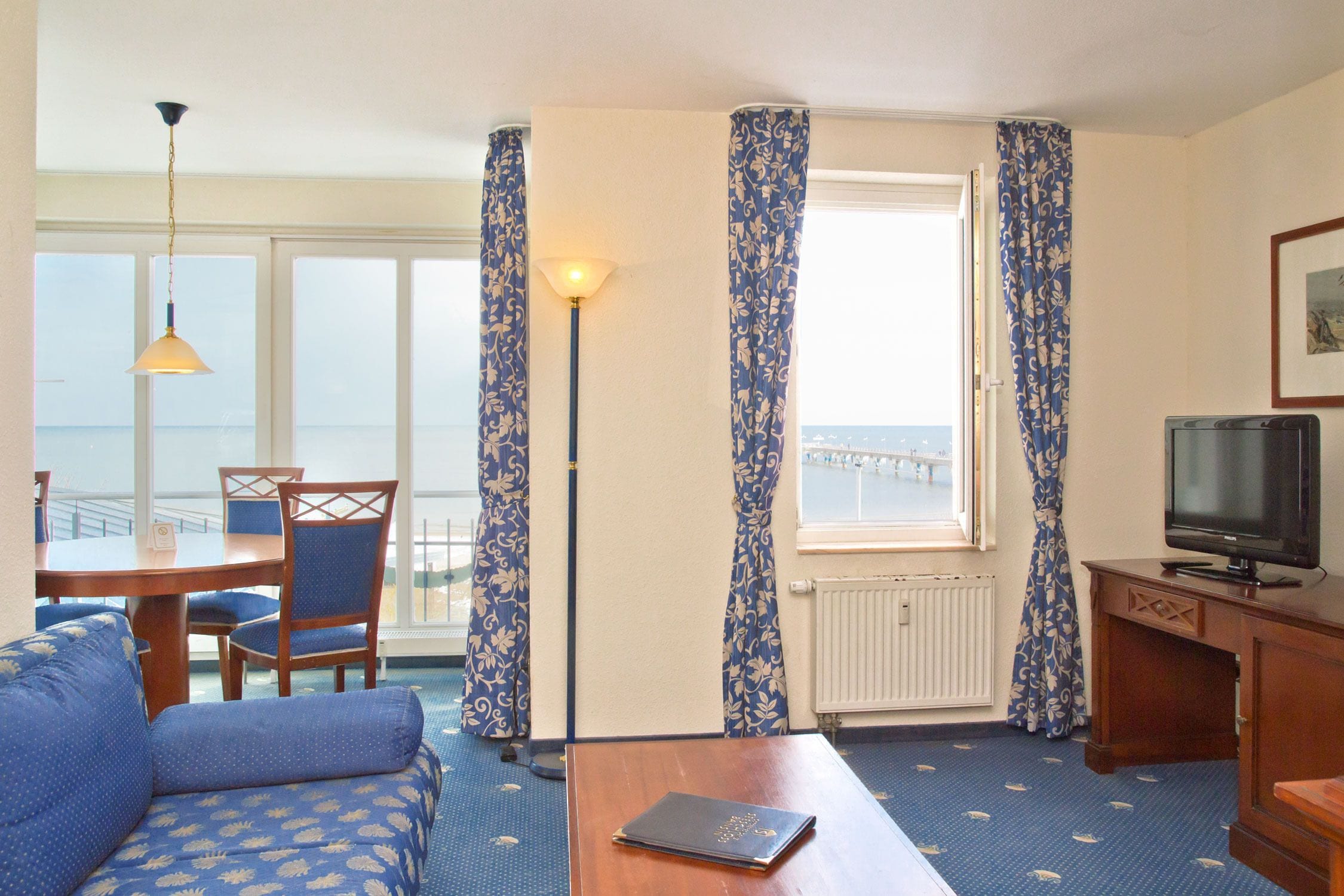Une chambre d’hôtel avec un canapé, une table à manger avec des chaises, un téléviseur et une fenêtre avec des rideaux.