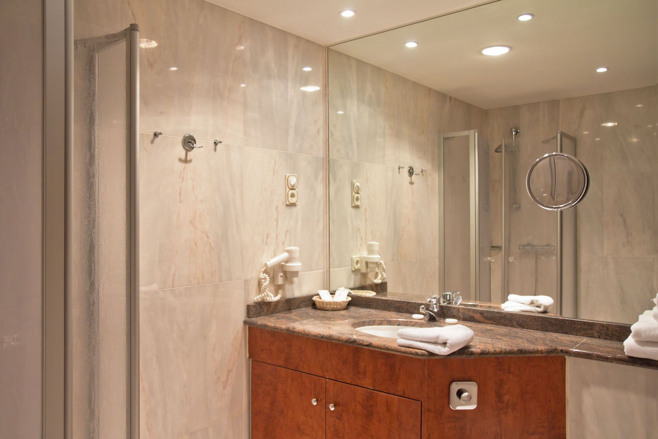 Un bagno moderno con un elegante mobile lavabo in marmo, un ampio specchio e una cabina doccia in vetro.