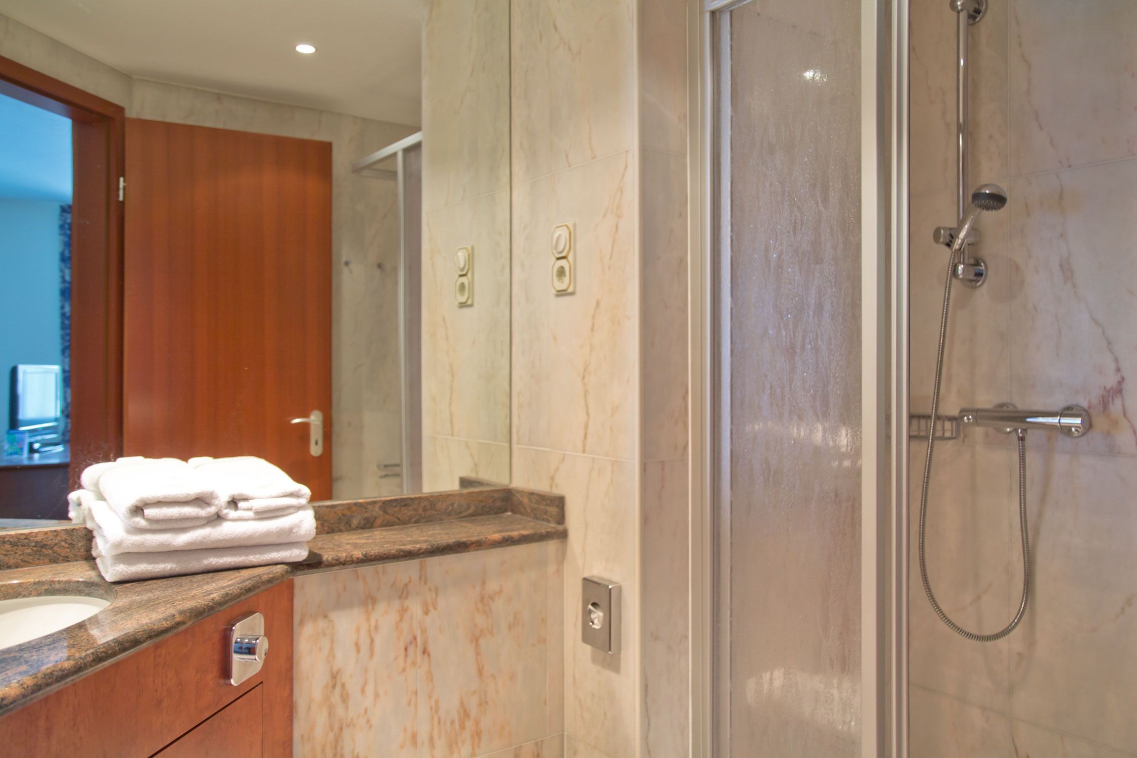 A modern bathroom with a marble countertop, a glass-enclosed shower, and a wooden door.