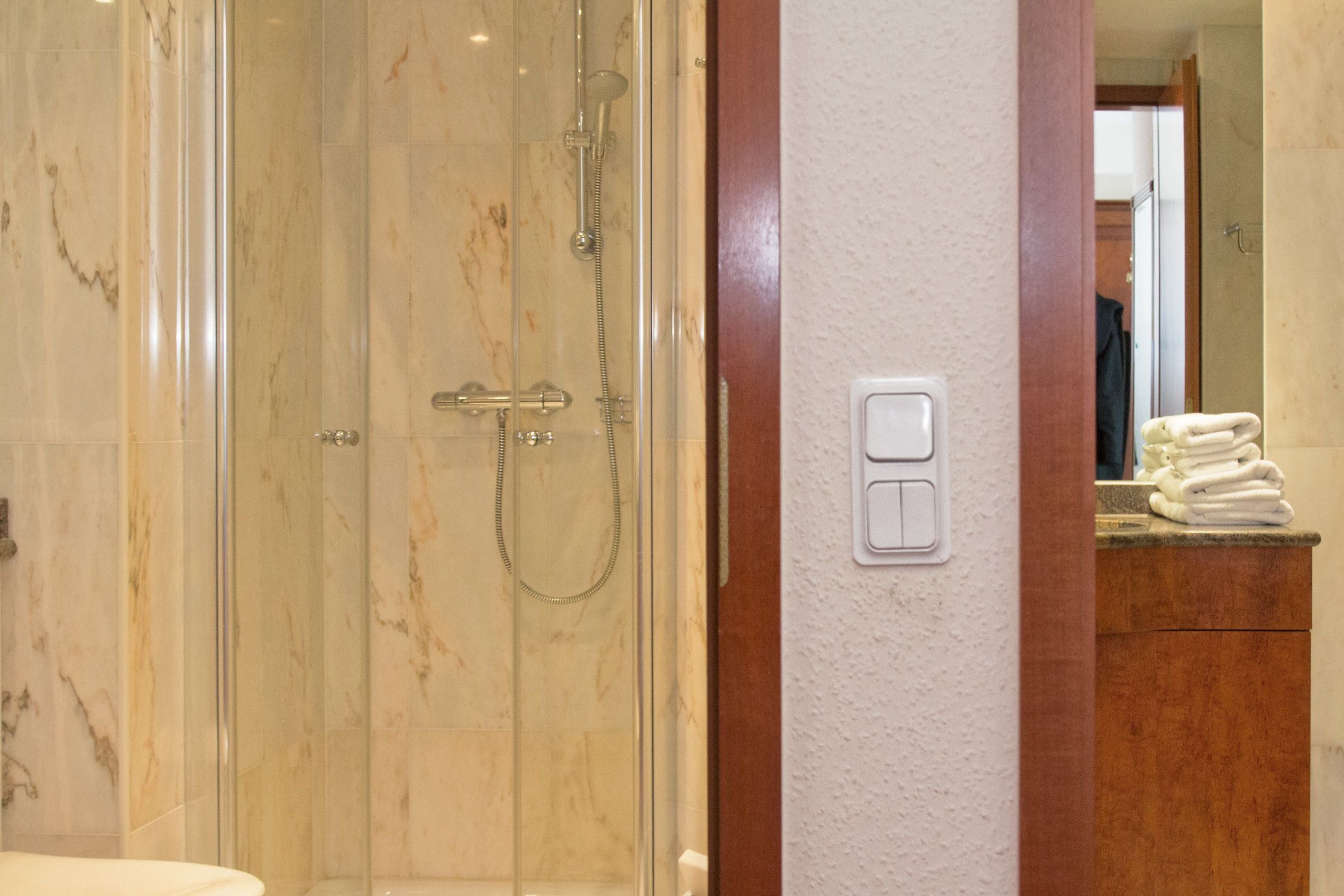 A bathroom with a glass-enclosed shower, a wooden vanity, and a towel rack.