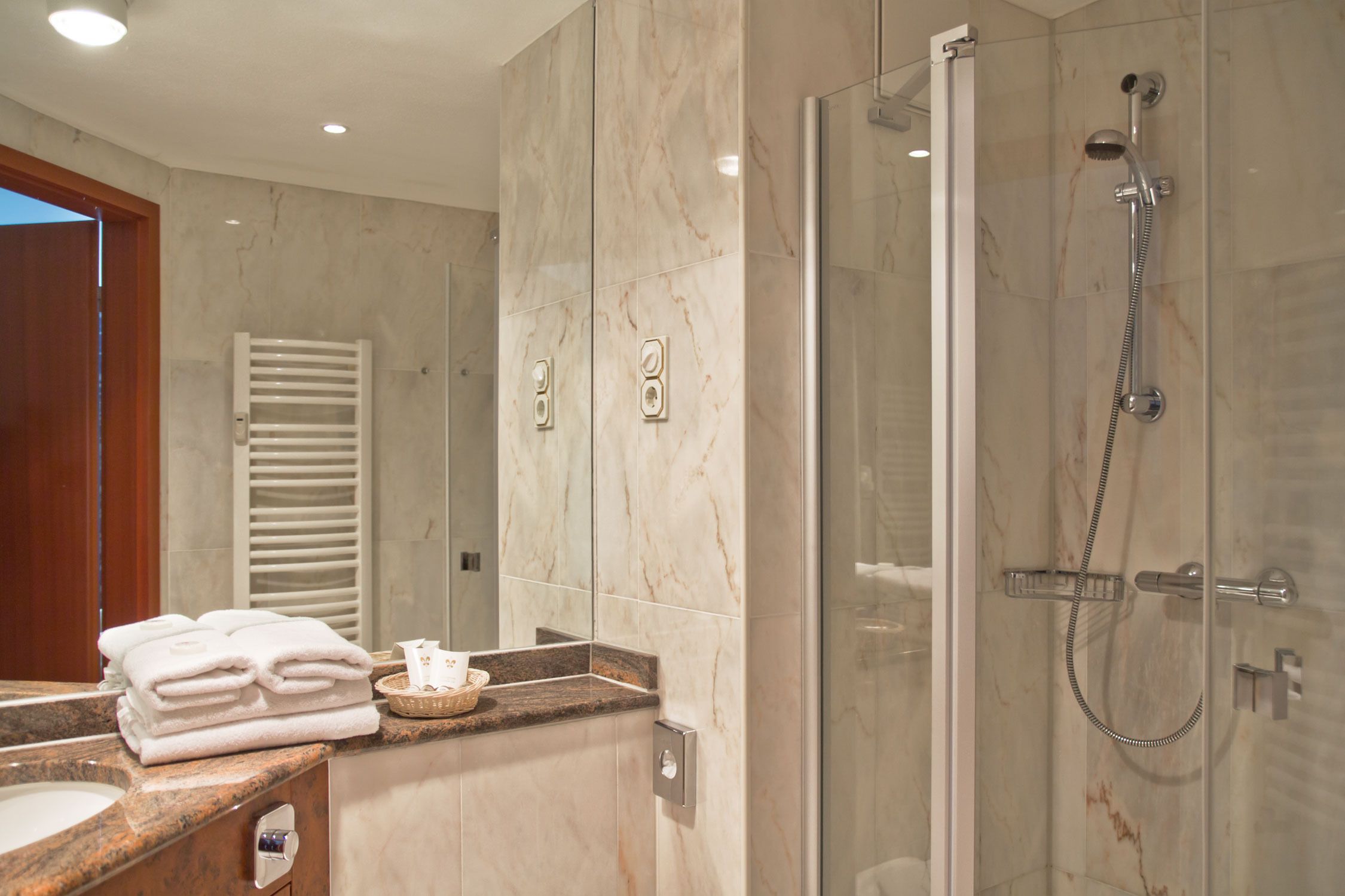 A modern bathroom with a glass-enclosed shower, marble walls, and a countertop with towels and toiletries.