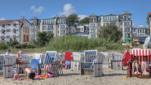 A beach with beach chairs and umbrellas, a building with multiple balconies, and a clear sky.