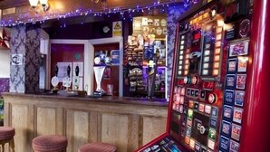 A bar area with wooden stools, a slot machine, and a bar counter with various items. - Emporium City Centre Self Catering (Nottingham)