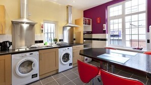 A modern kitchen with stainless steel appliances, a washing machine, and a dining area with red chairs. - Emporium City Centre Self Catering (Nottingham)