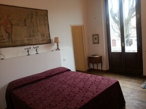 A room with a bed, a painting on the wall, a lamp, a small table, and a door leading outside. - Little Garden Donatello (Florence)