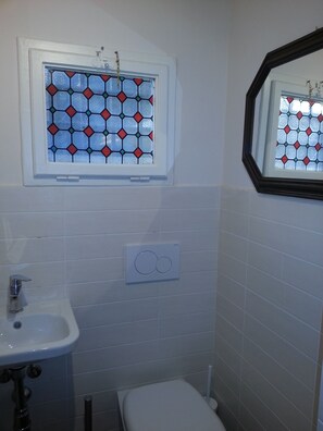 A bathroom with a white sink, a toilet, and a window with a stained glass design. - Little Garden Donatello (Florence)