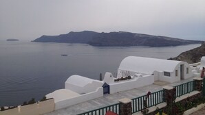 A coastal view with white buildings, a calm sea, and a distant island. - Stelios Rooms (Santorini)