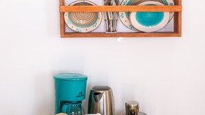 A kitchen area with a wooden shelf holding dishes and utensils, a coffee maker, and a kettle on a countertop. - Stelios Rooms (Santorini)
