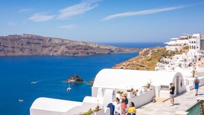 A coastal view with white buildings, a clear blue sky, and the sea. - Stelios Rooms (Santorini)