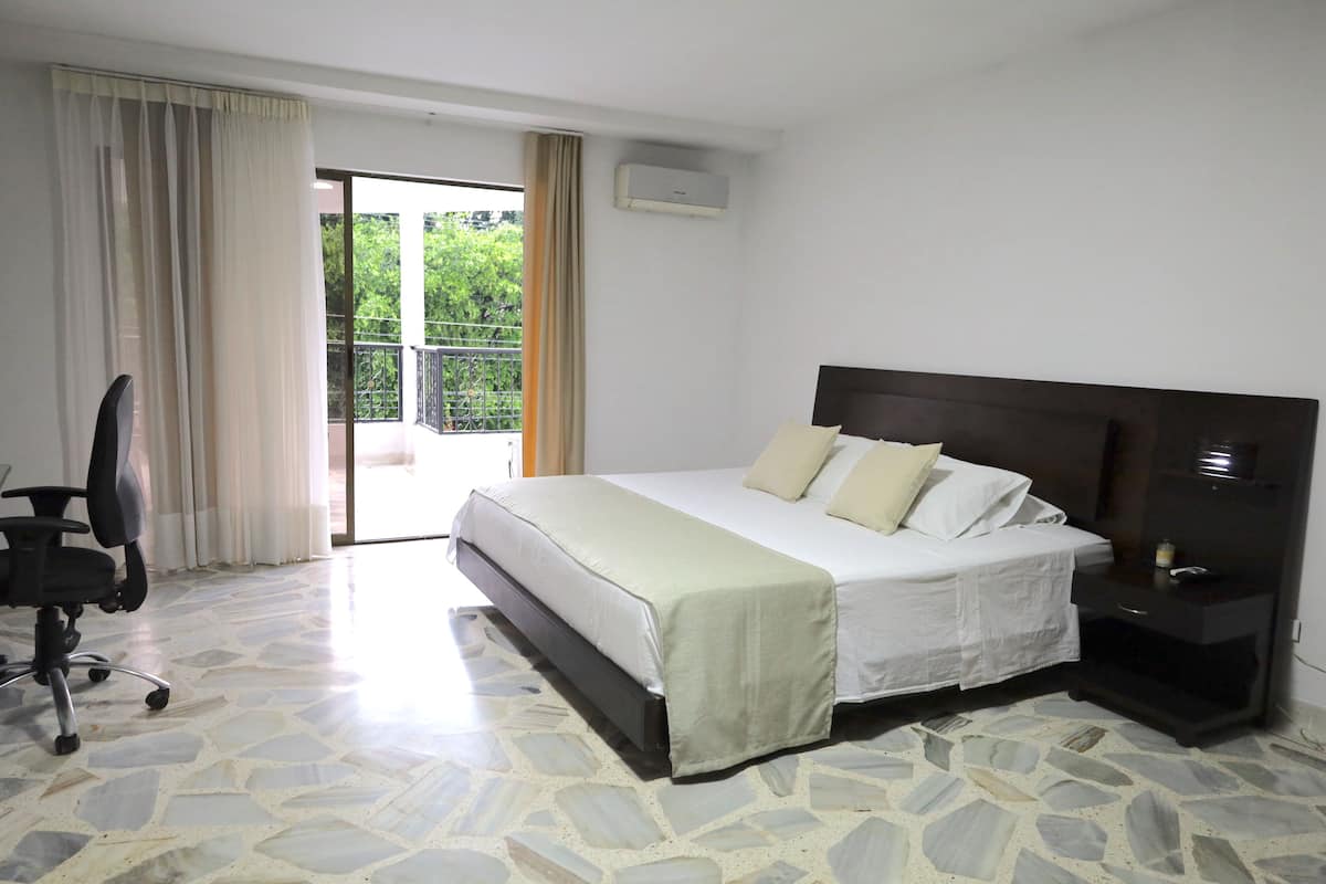 A hotel room with a bed, a chair, a nightstand, and a balcony with curtains.