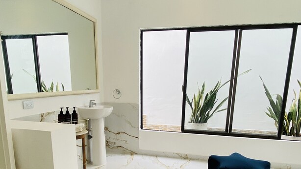 Ein geräumiges Badezimmer mit großem Spiegel, Waschbecken und Fenster mit Pflanzen.