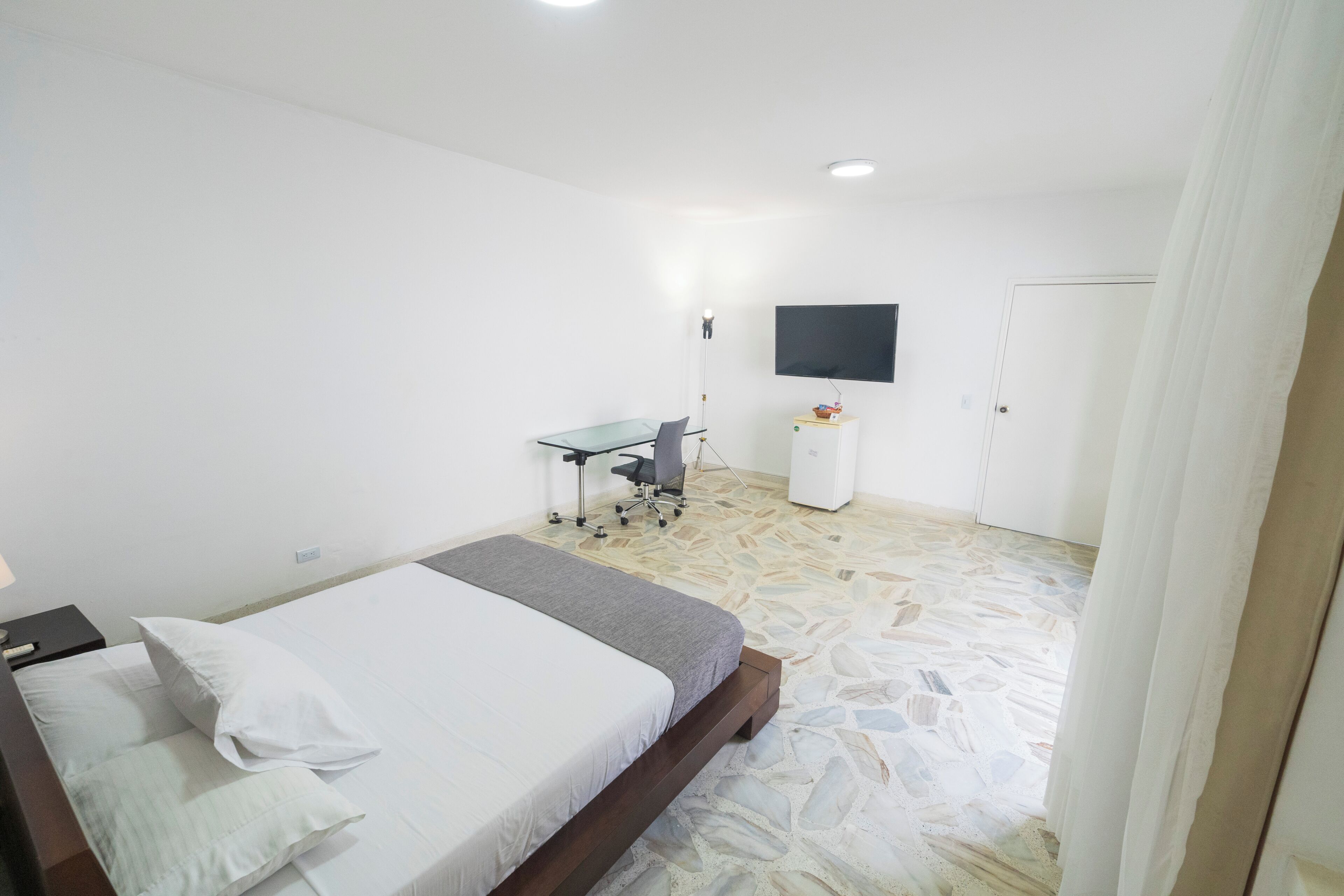 A bedroom with a bed, a desk, a chair, a TV, and a wardrobe.