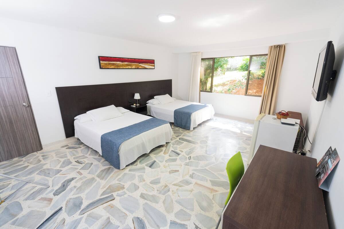 A hotel room with two beds, a TV, a desk, and a window with curtains.