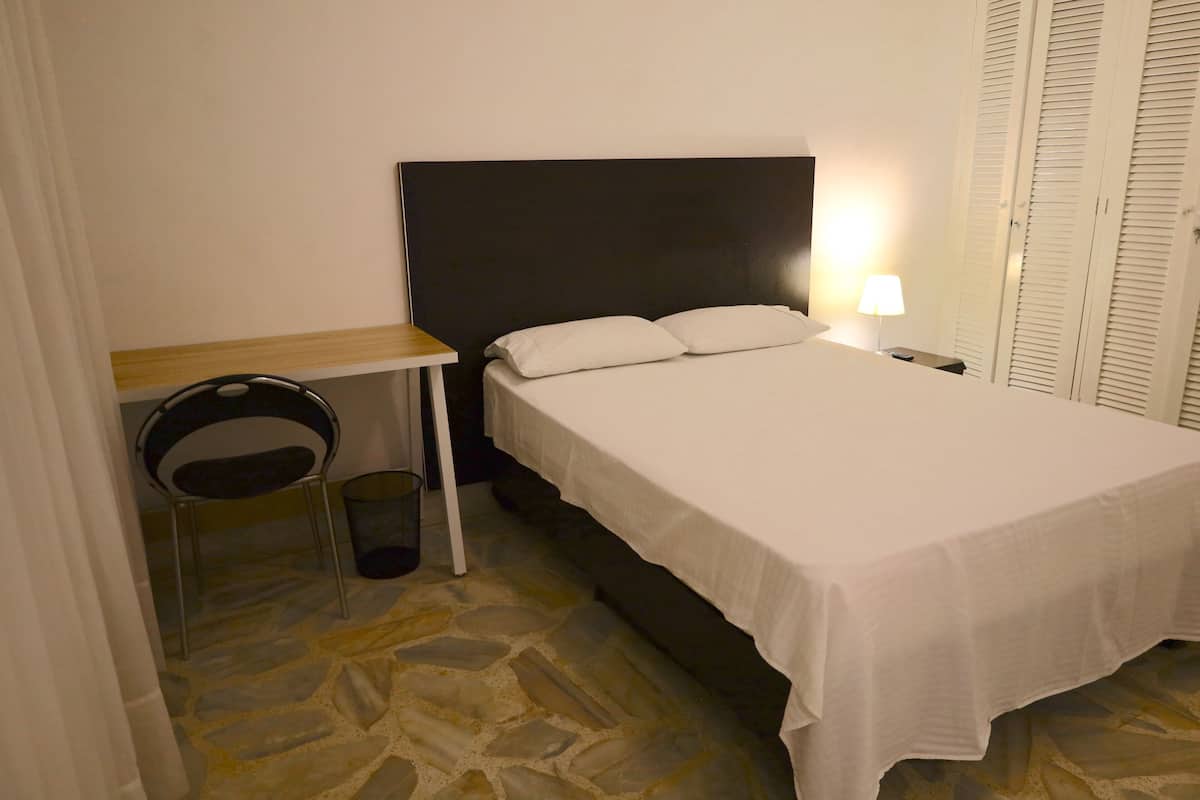 A bedroom with a bed, a desk, a chair, and a lamp.