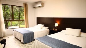 Ein Hotelzimmer mit zwei Betten, einem Fenster mit Vorhängen, einer Klimaanlage und einem Nachttisch mit Lampe.