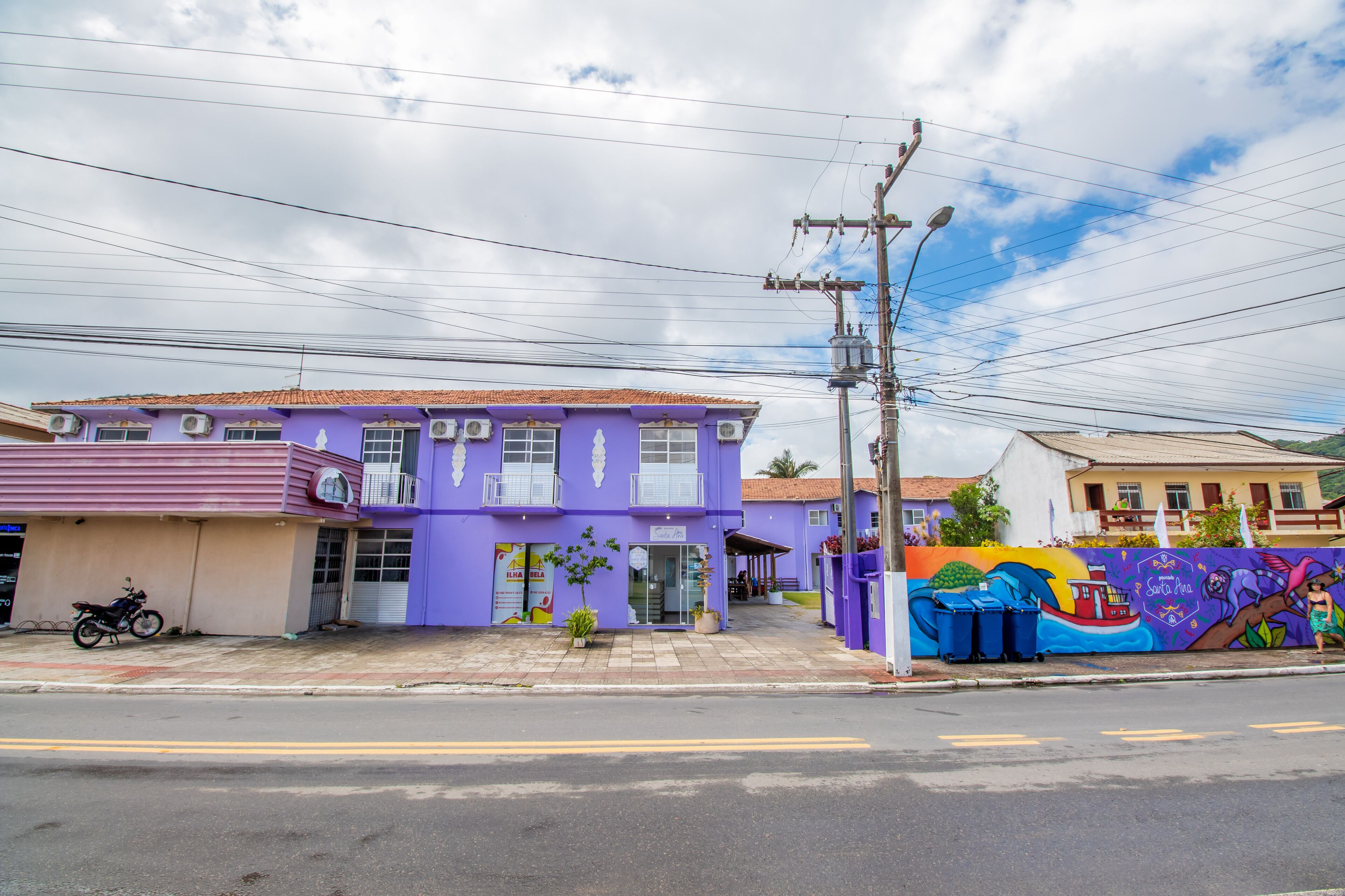 A purple building with a storefront, a motorcycle parked outside, and a colorful mural on the adjacent wall.