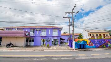 A purple building with a storefront, a motorcycle parked outside, and a colorful mural on the adjacent wall.