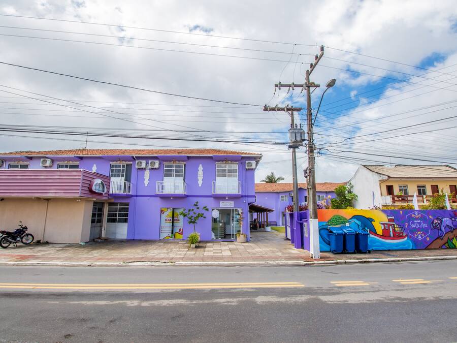 A purple building with a storefront, a motorcycle parked outside, and a colorful mural on the adjacent wall.