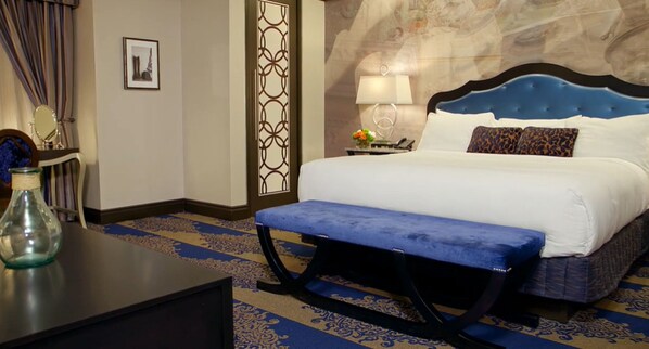 Una habitación de hotel con cama, banca, mesita de noche, lámpara, espejo y un panel decorativo en la pared.