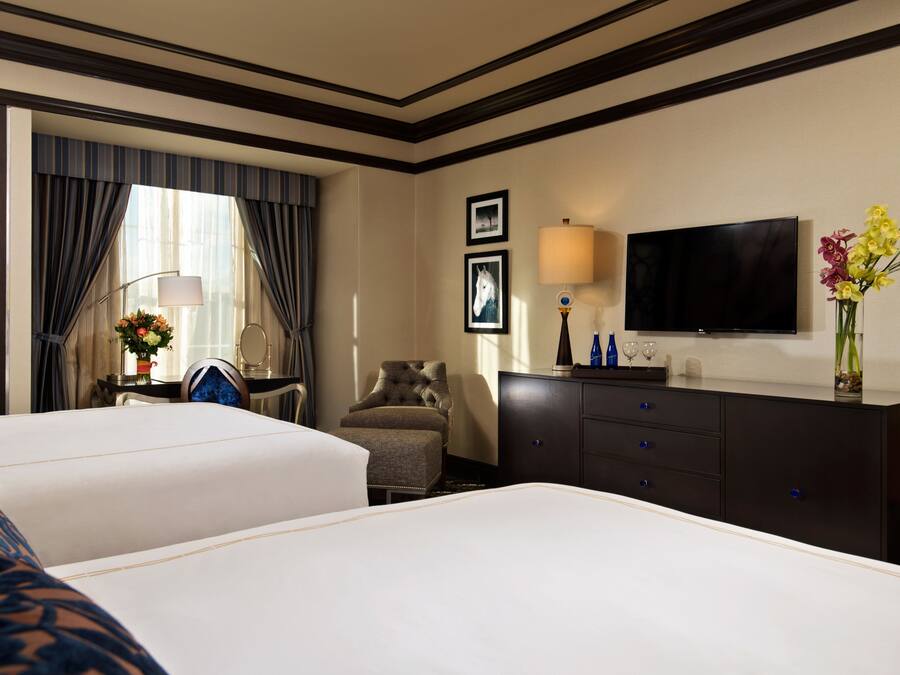 A hotel room with two beds, a TV, a desk with a lamp, and a chair.