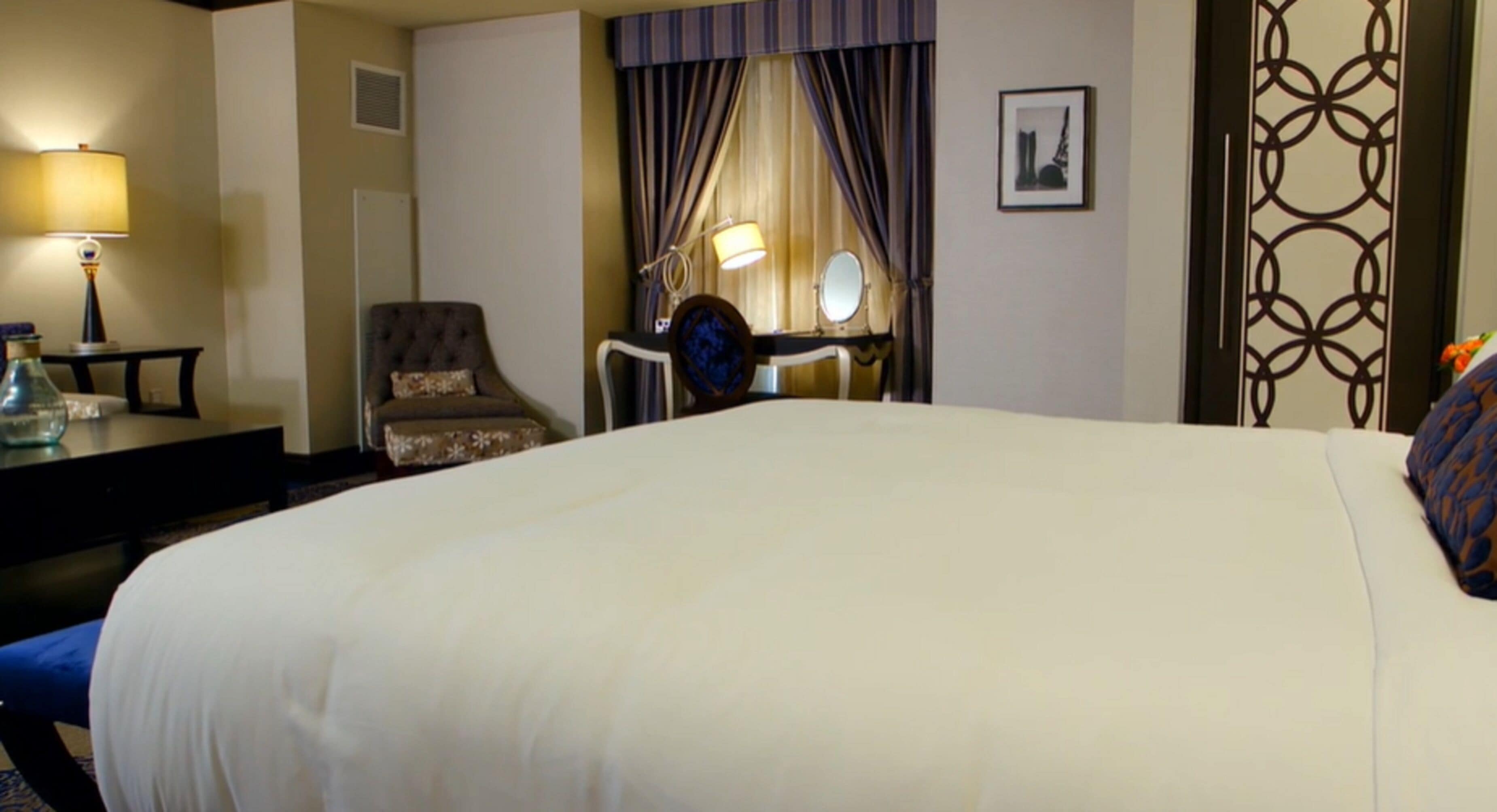 A hotel room with a large bed, a desk with a lamp, a chair, and a mirror.