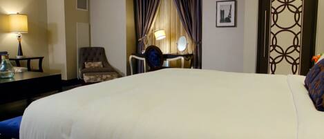 Una habitación de hotel con una cama grande, un escritorio con lámpara, una silla y un espejo.