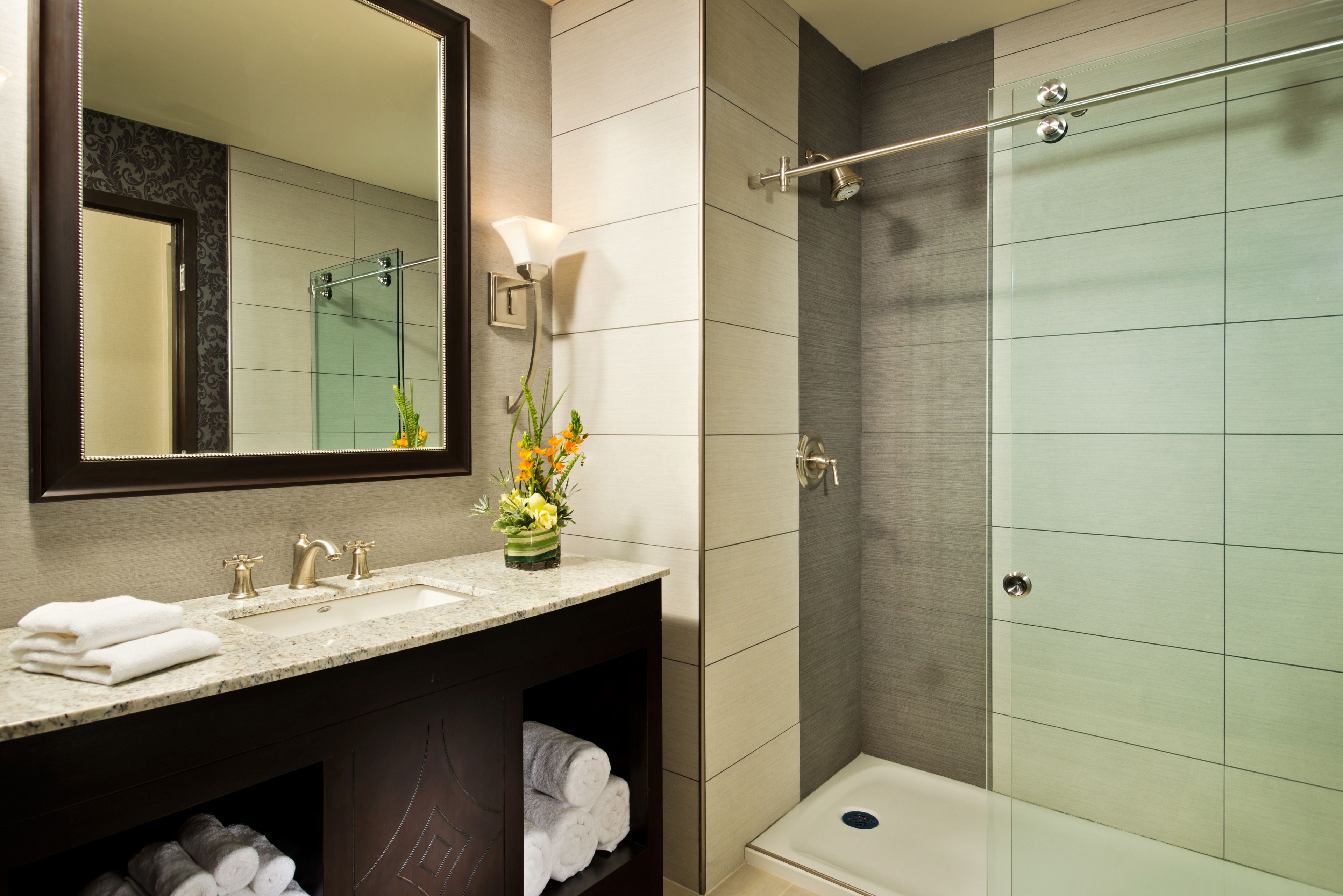 Une salle de bain moderne avec un lavabo en marbre, une cabine de douche en verre et un miroir agrémenté d’un luminaire fixé au mur.