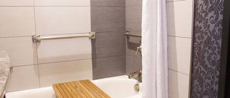 A bathroom with a bathtub, wooden bath mat, grab bars, and a shower curtain.