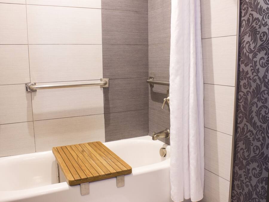 A bathroom with a bathtub, wooden bath mat, grab bars, and a shower curtain.
