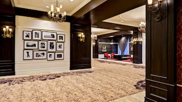 A spacious lobby with a patterned carpet, framed photographs on the wall, and a seating area with red chairs.