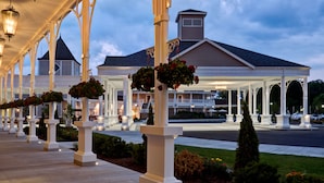 A covered walkway with white columns and hanging flower baskets, leading to a building with a dark roof. - Saratoga Casino Hotel (Saratoga Springs)