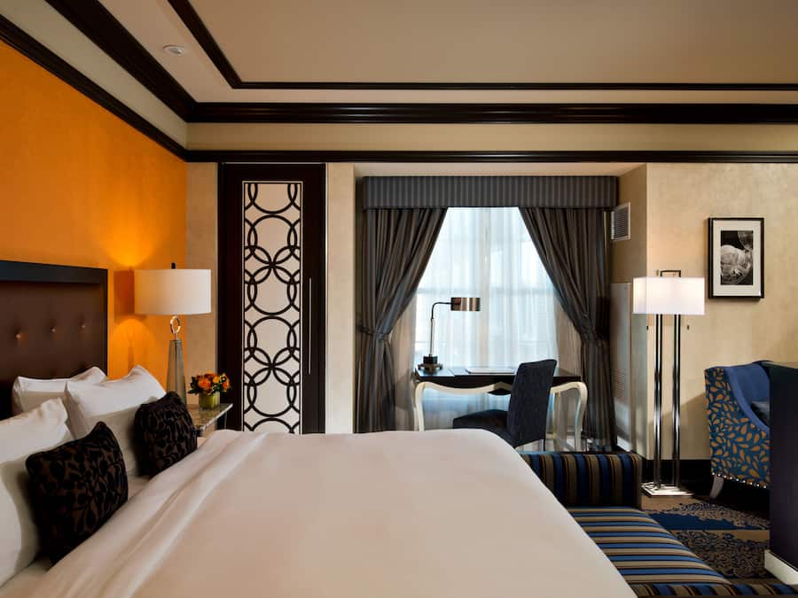 A hotel room with a large bed, a desk, a chair, and a desk lamp.