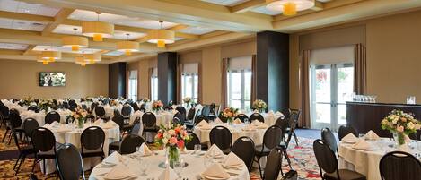 A banquet hall with round tables set for dining, equipped with chairs, table settings, and floral centerpieces.