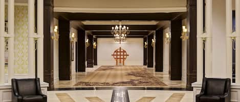 Un hall imponente con candelabro, columnas decorativas y alfombra estampada.