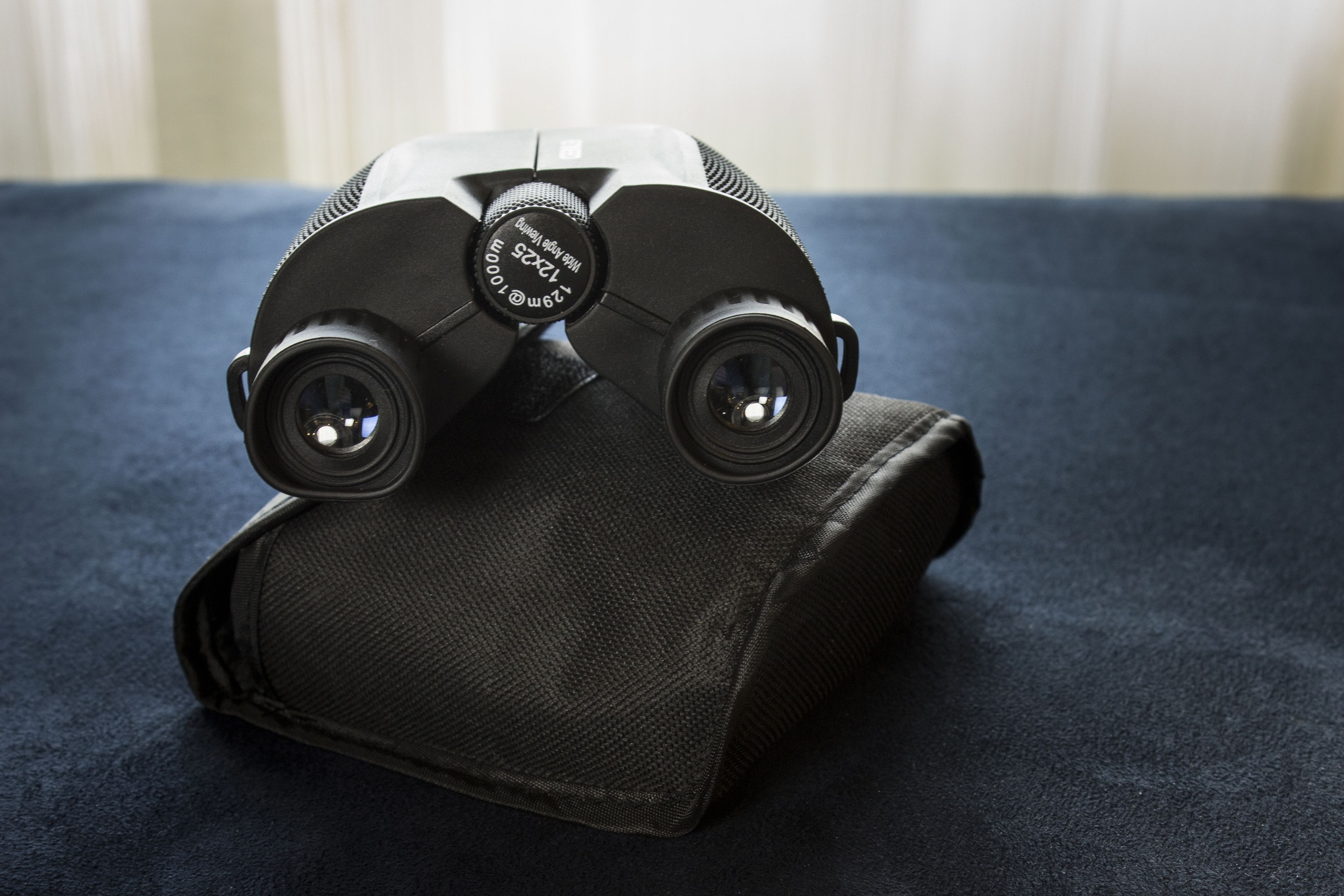A pair of binoculars with a focus ring and a strap, placed on a textured fabric surface.