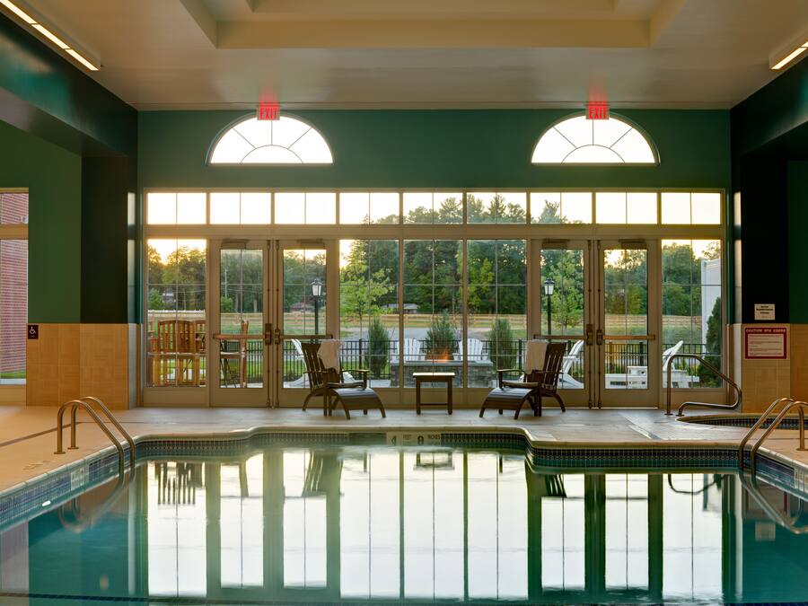 Una piscina interior con paredes de vidrio transparente, dos sillas de descanso y una mesa.