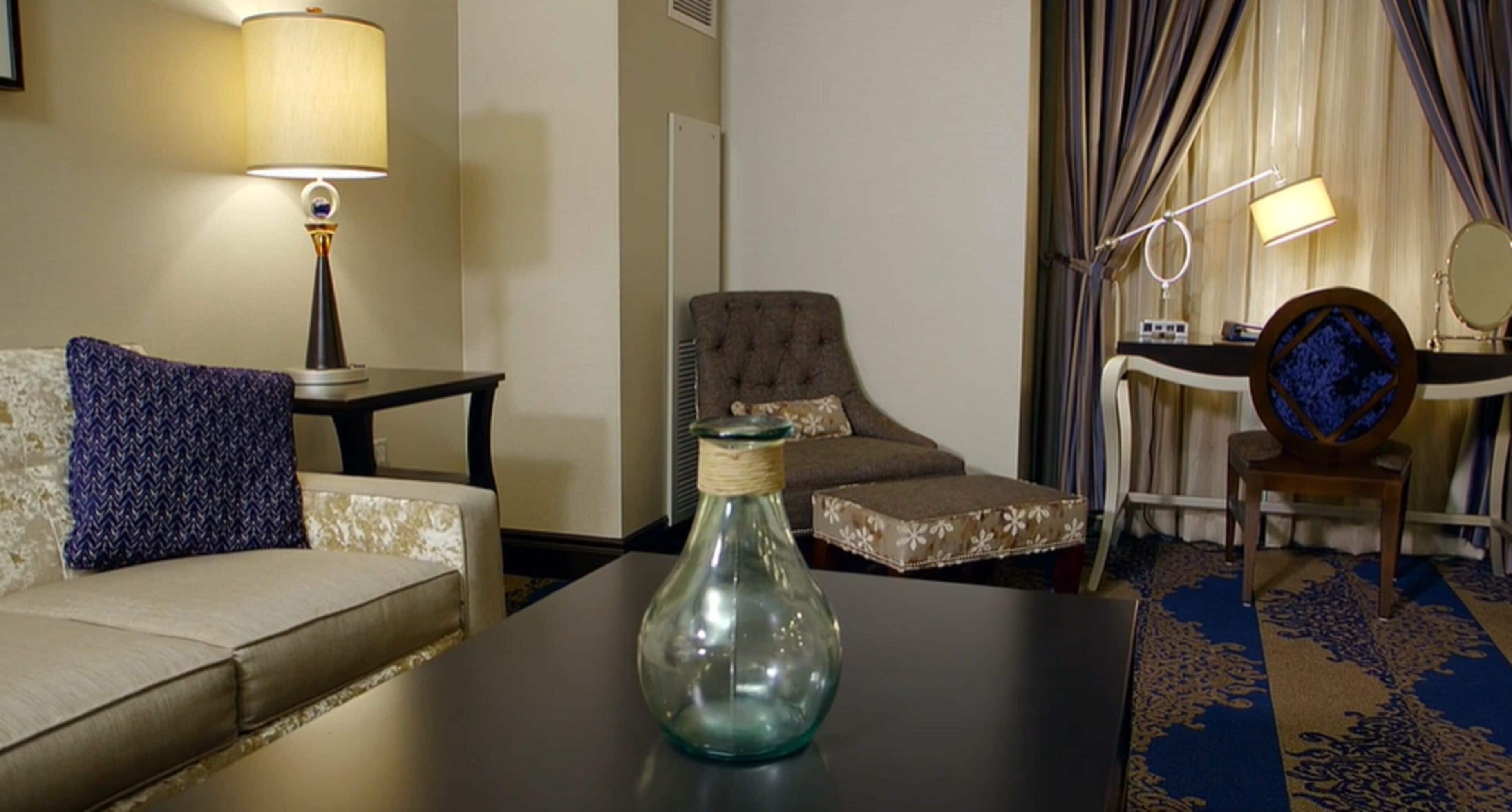 A hotel room with a sofa, a chair, a small table with a vase, a lamp, a mirror, and a bed with curtains.