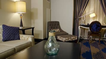 Habitación de hotel con sofá, una silla, una mesita con un florero, lámpara, espejo y cama con cortinas.