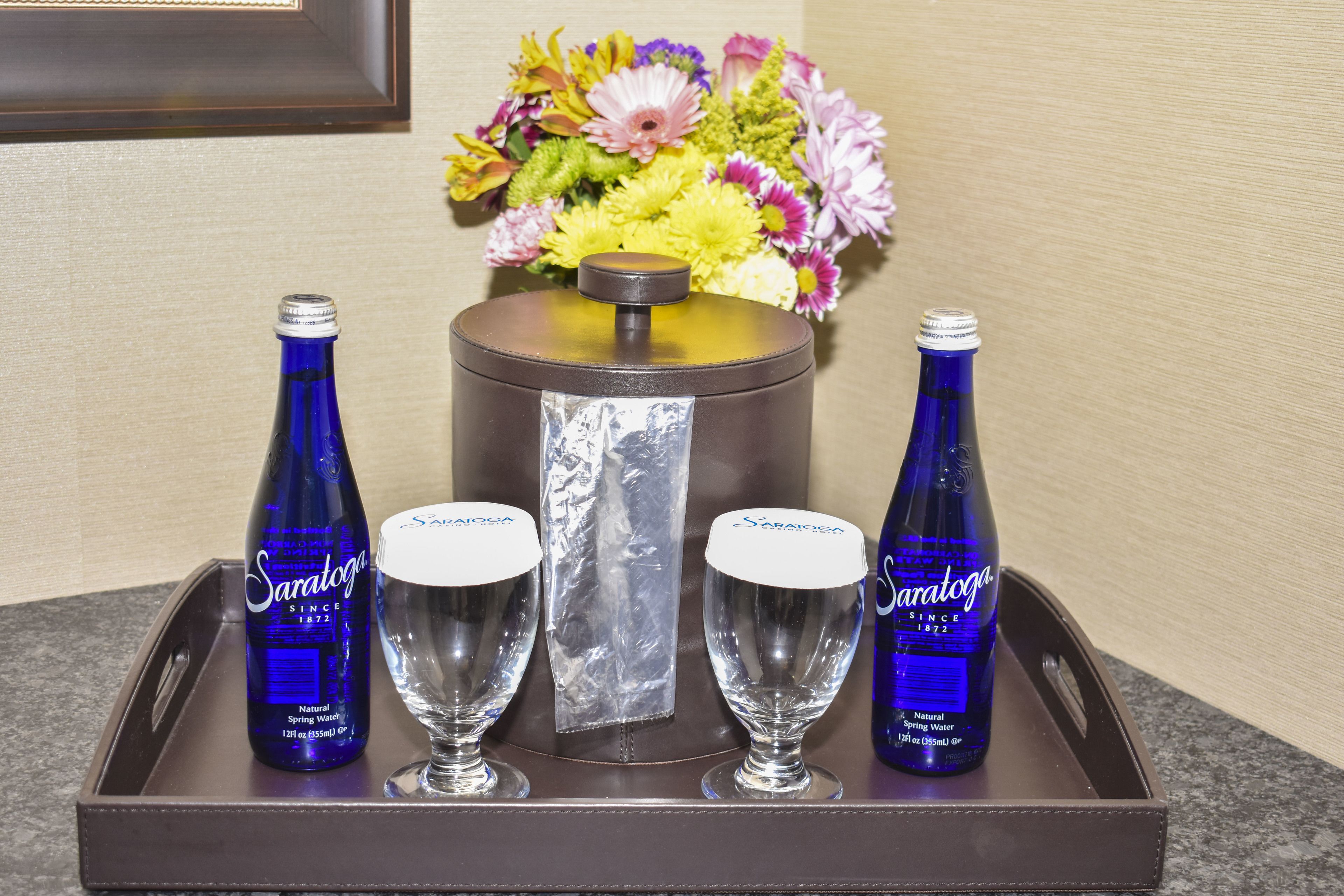 Un plateau avec deux bouteilles d’eau de source de Saratoga, deux verres et un bouquet de fleurs.