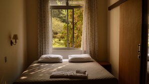 Una cama bien hecha con almohadas y una toalla doblada, una lámpara de noche y una ventana con cortinas.