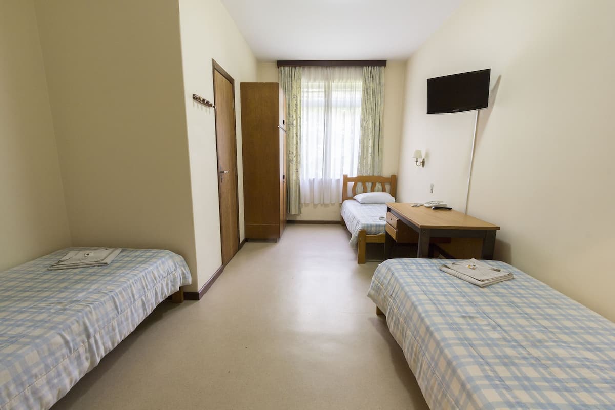 A small, clean room with two single beds, a desk, a chair, a television, and a window with curtains.
