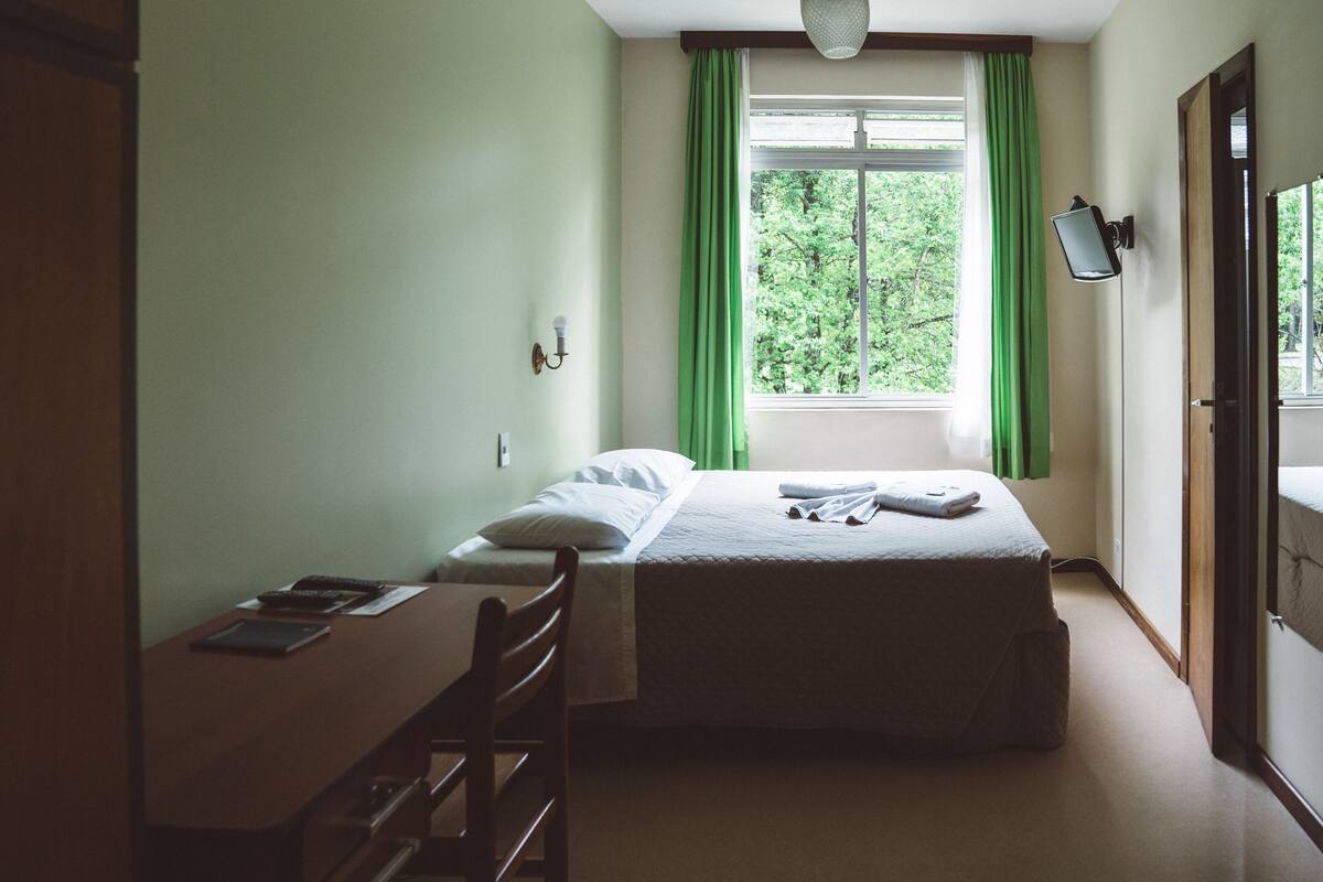 A bedroom with a bed, a desk, and a window with curtains.
